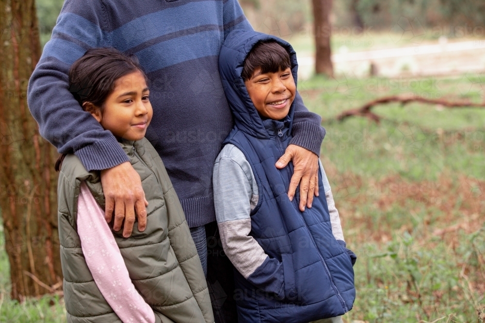 Close up shot of a boy wearing blue coat and a girl wearing green coat being held by man on a field - Australian Stock Image