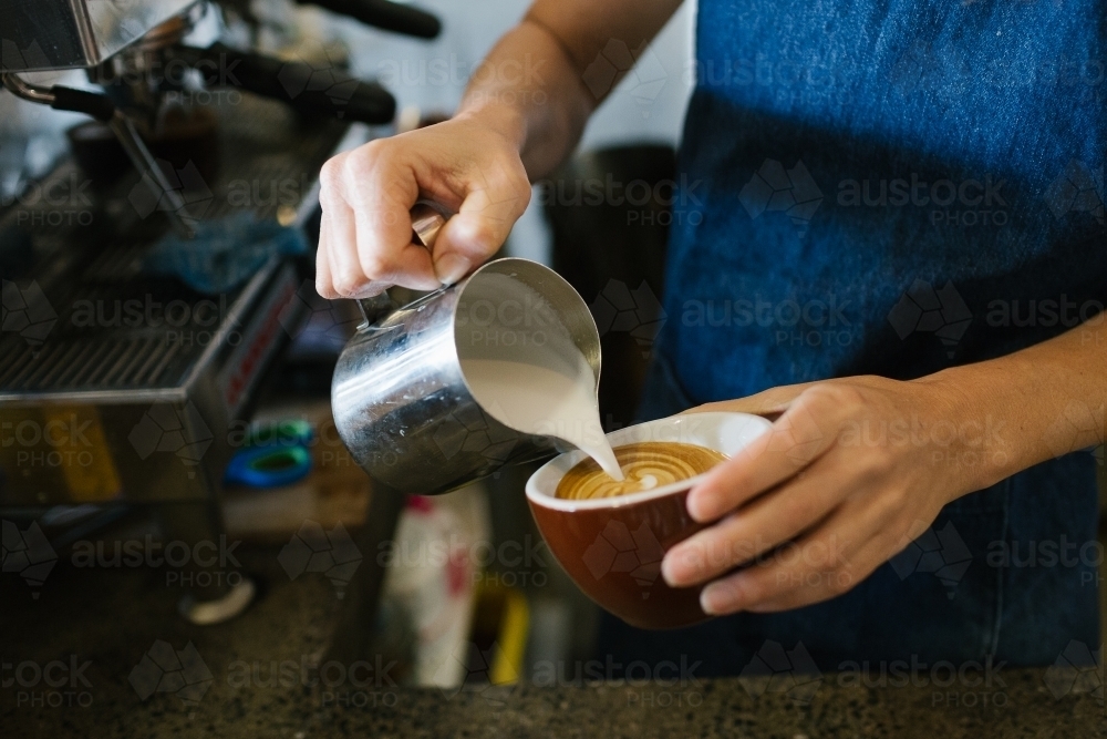 Close up shot of a man's holding a cup of coffee also pouring milk in a tin mug to the coffee - Australian Stock Image