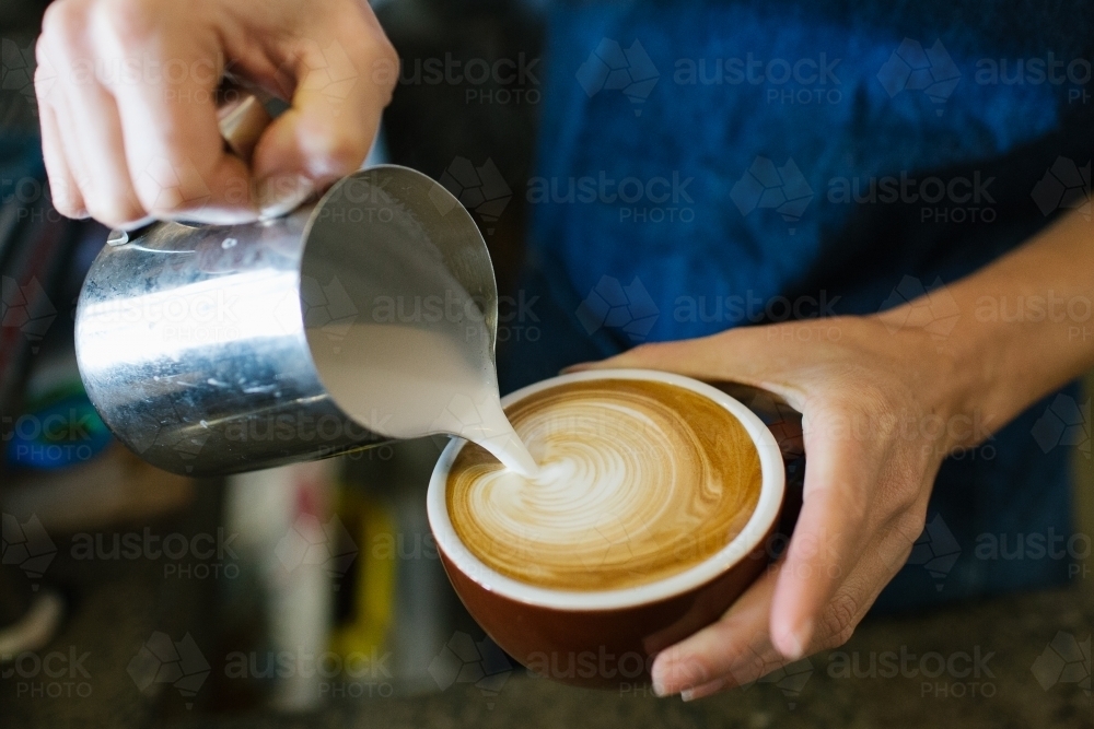 Close up shot of a man's holding a cup of coffee also pouring milk in a tin mug to the coffee - Australian Stock Image