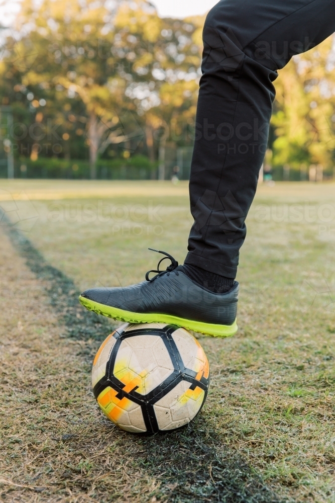 Close up shot of a man stepping on a soccer ball with one foot on the field - Australian Stock Image