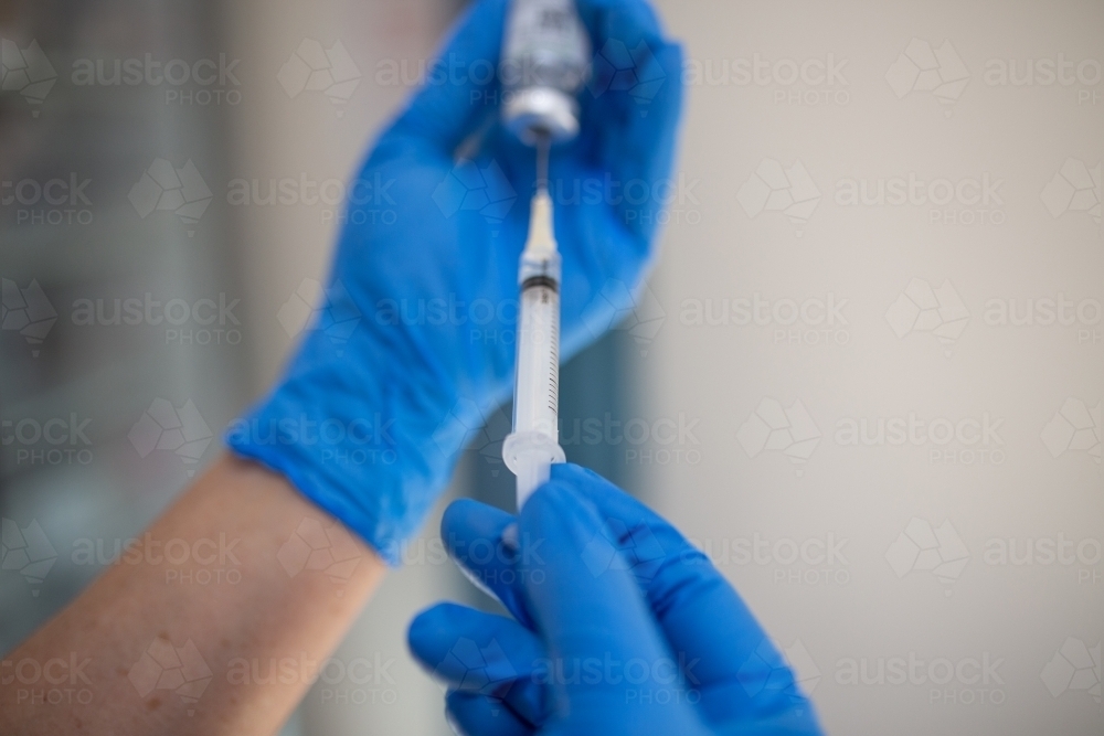 Close up shot of a syringe being inserted to a medicine glass vial by a healthcare worker - Australian Stock Image