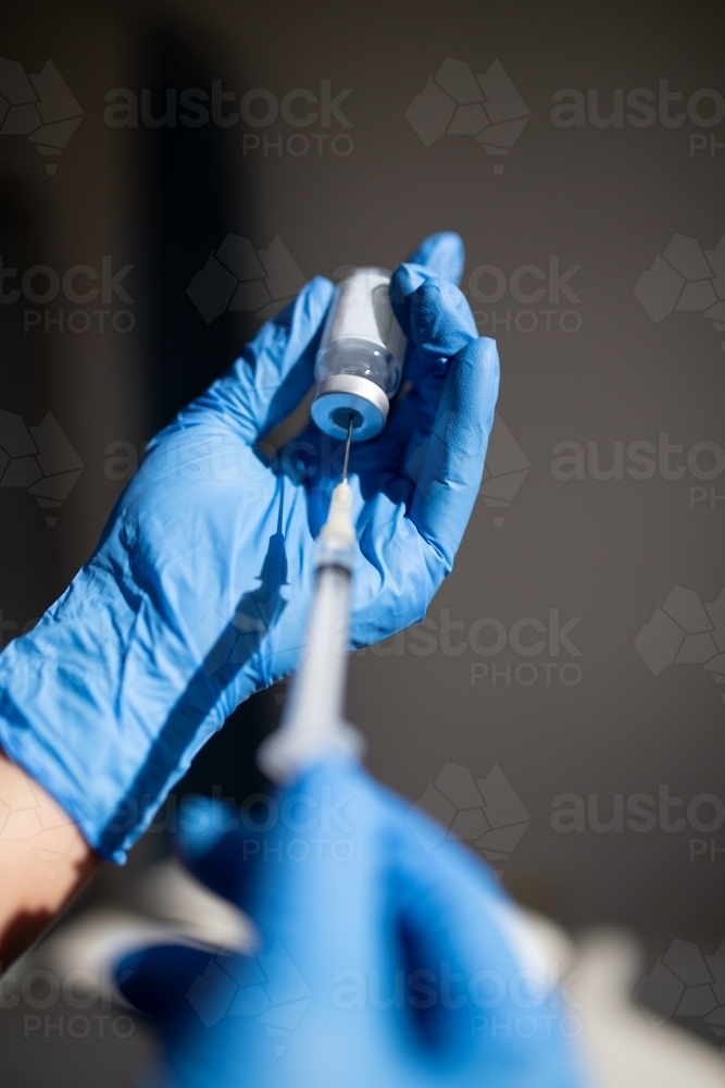 Close up shot of a syringe being inserted to a medicine glass vial by a healthcare worker - Australian Stock Image