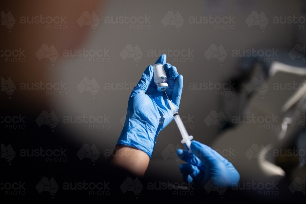 Close up shot of a syringe being inserted to a medicine glass vial by a healthcare worker - Australian Stock Image