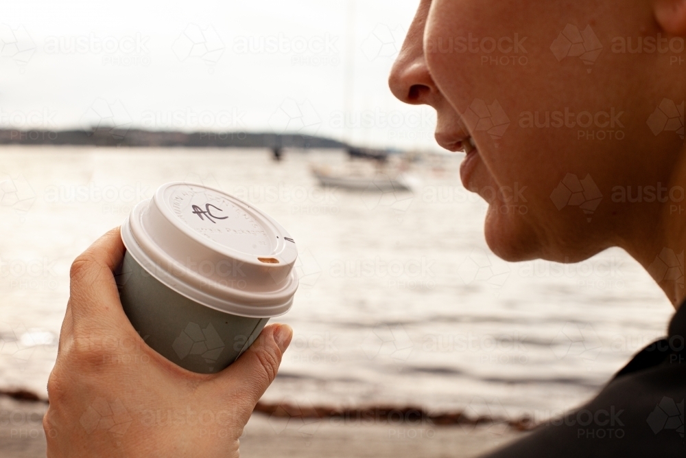 close up shot of a woman holding a cup of coffee with initials AC by the beach - Australian Stock Image