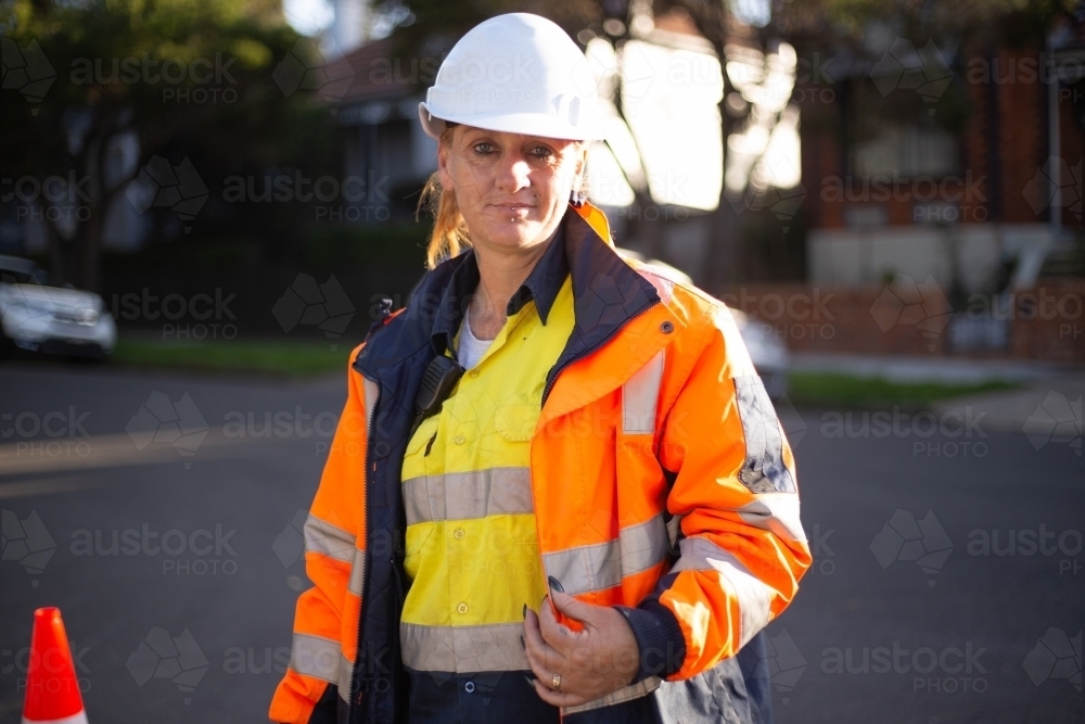 Close up shot of a woman road worker with white helmet and orange jacket with a silver reflector - Australian Stock Image