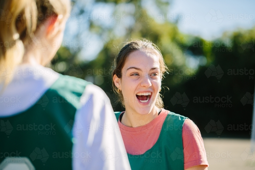 close up shot of a young woman smiling with mouth open with another woman blurred in the foreground - Australian Stock Image