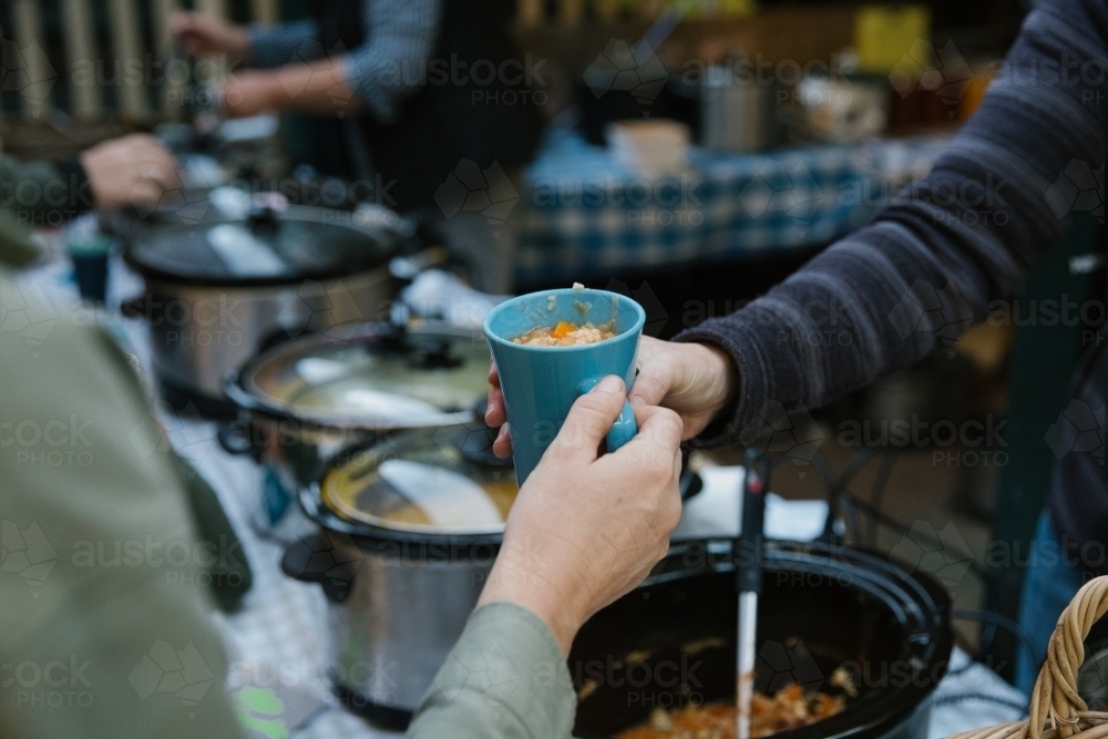 Close up shot of blue green cup with food inside being passed to another person - Australian Stock Image