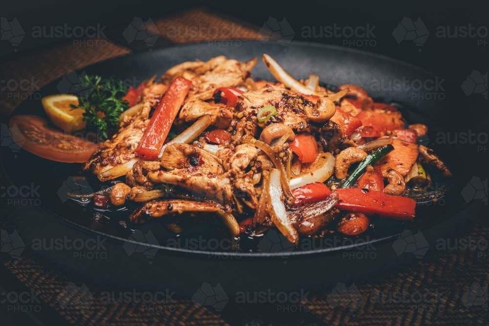 Close up shot of cashew nut chicken in a black plate - Australian Stock Image