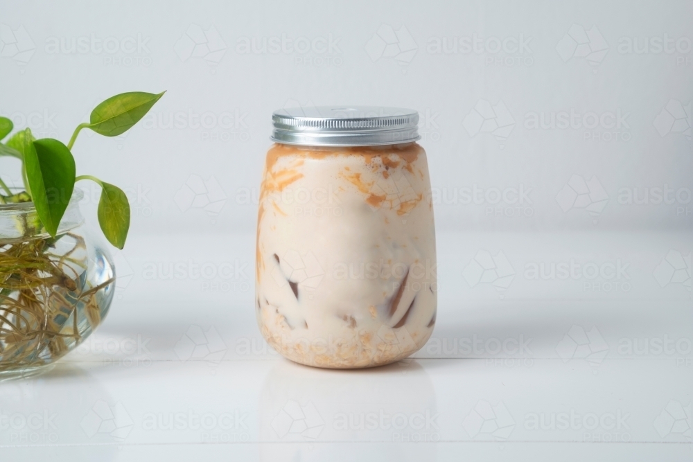 Close up shot of peanut butter protein smoothie in a jar with a plant on the side - Australian Stock Image