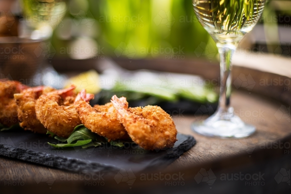 Close up shot of shrimp tempura on a black plate with a blurred background of a platter and glass - Australian Stock Image