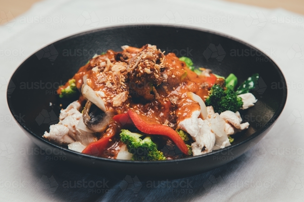 Close up shot of thai stir fry peanut chicken in black bowl - Australian Stock Image