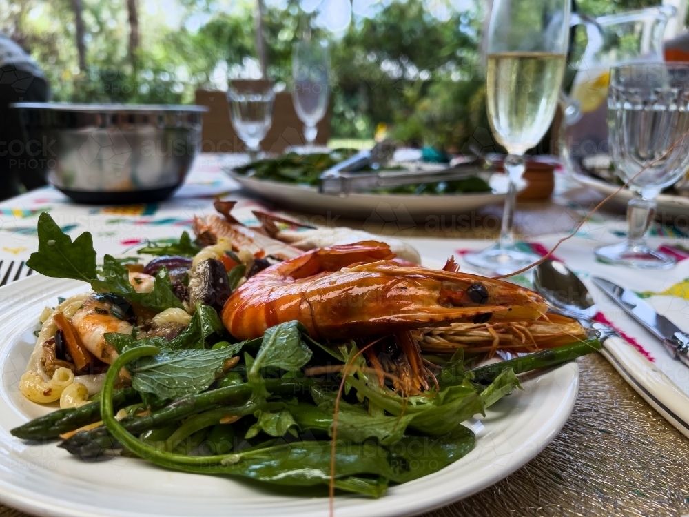 Close view of tiger prawns and wilted greens on a plate with table setting and wine glasses - Australian Stock Image