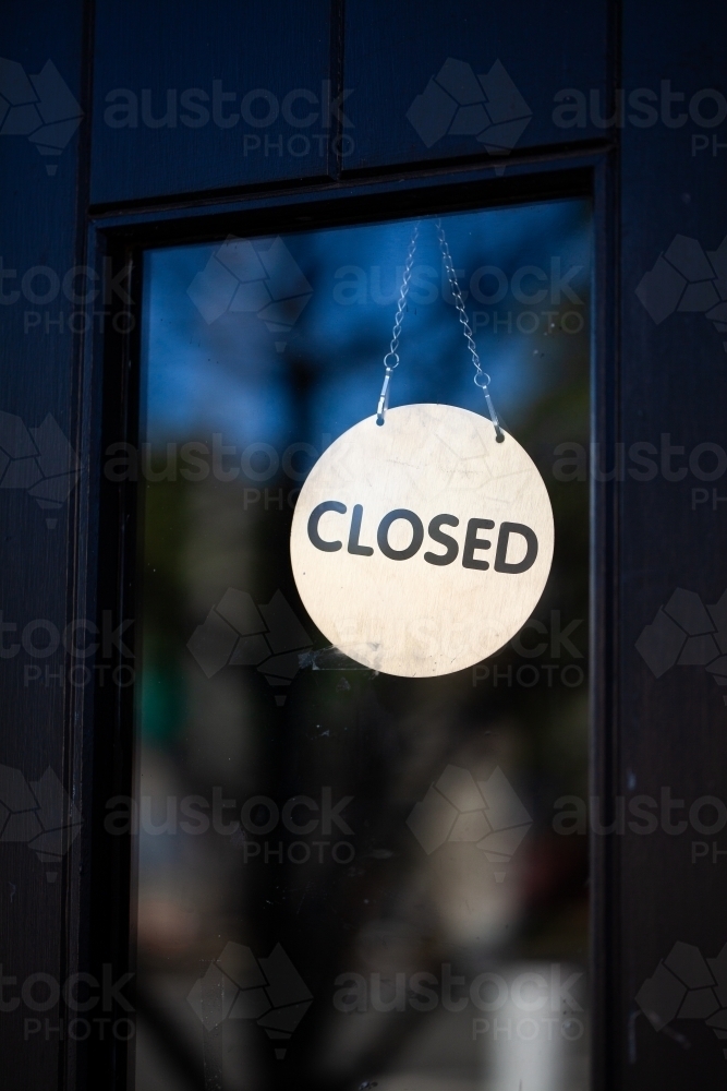 Closed sign hanging in glass pane of shop front door - Australian Stock Image