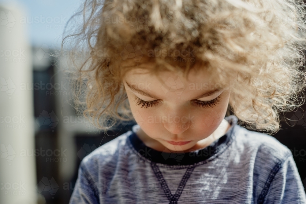 Closeup portrait of a young boy with messy curly hair looking down - Australian Stock Image