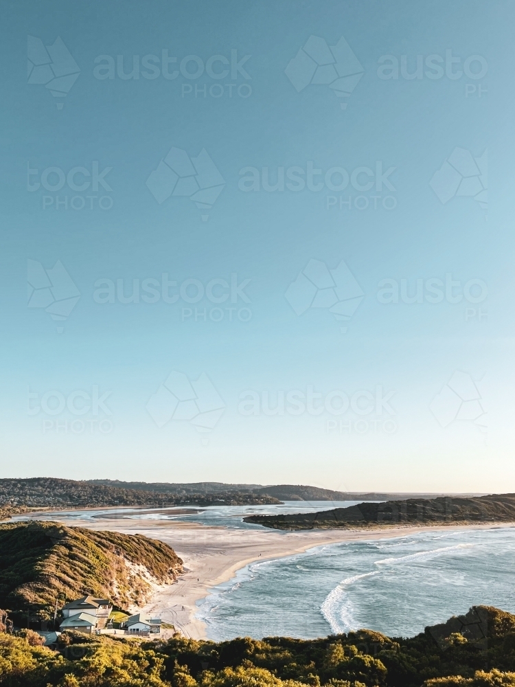 Coastal long shot of bay meeting river mouth with surf club buildings on beach - Australian Stock Image