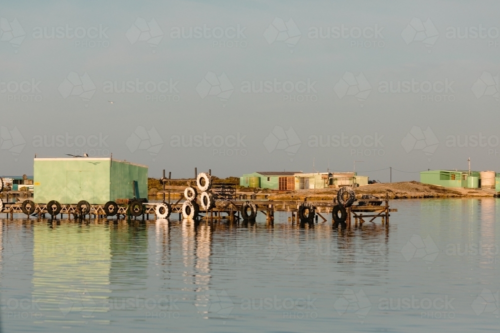 Colourful fishing shacks and sheds with wooden jetty and water reflections - Australian Stock Image