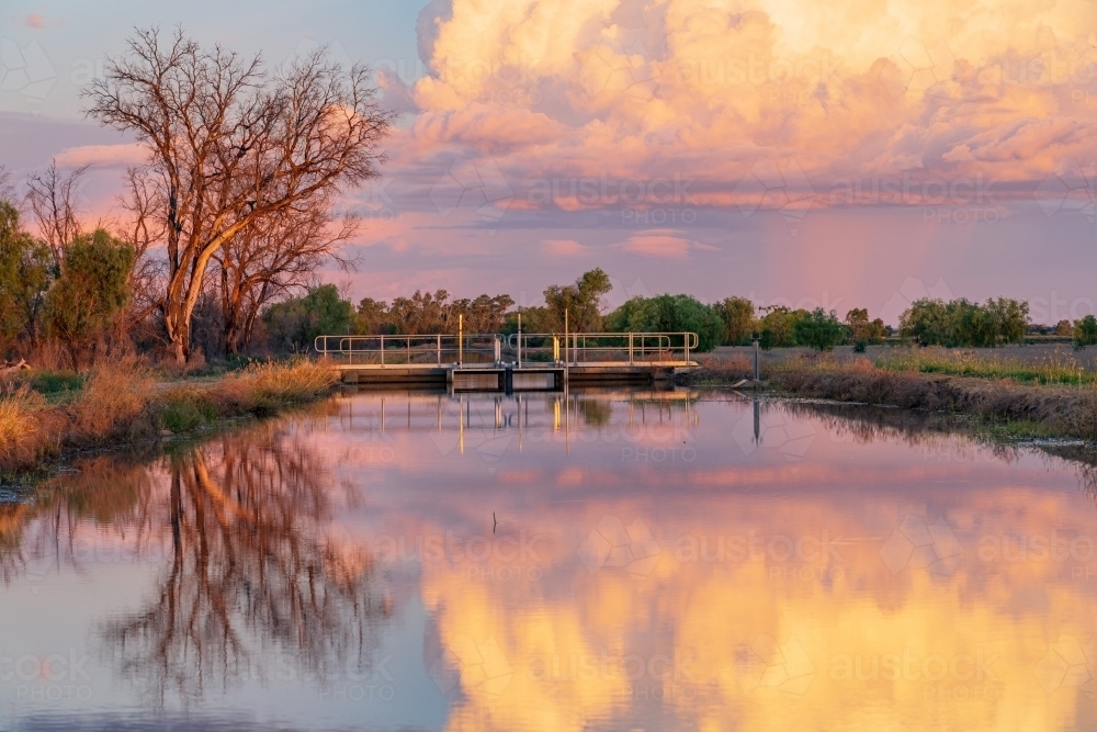 Colourful storm clouds at twilight reflected in the water of an irrigation channel - Australian Stock Image