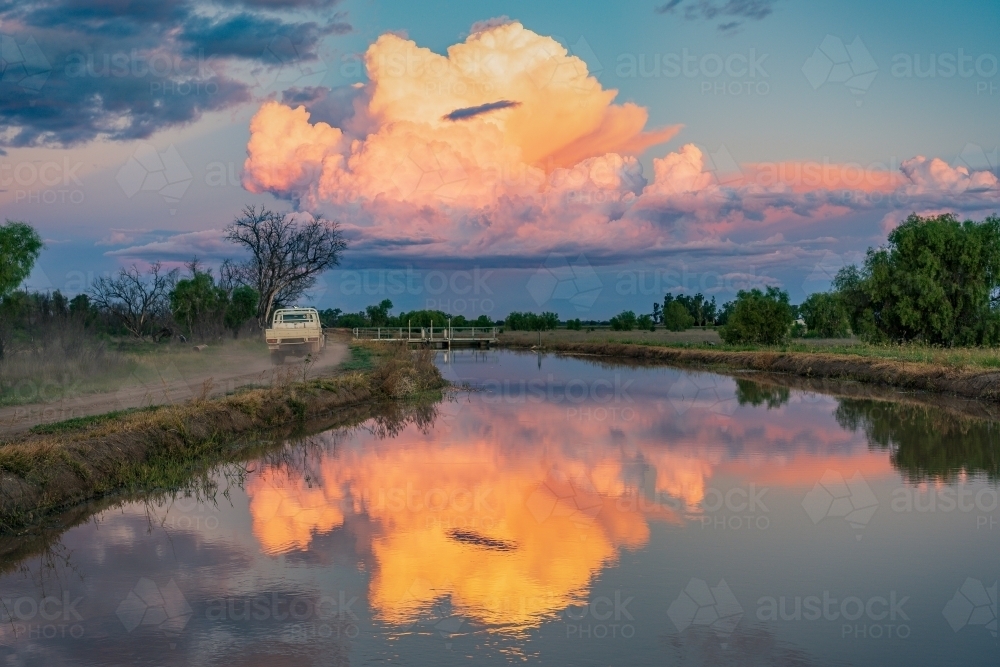 Colourful storm clouds at twilight reflected in the water of an irrigation channel - Australian Stock Image