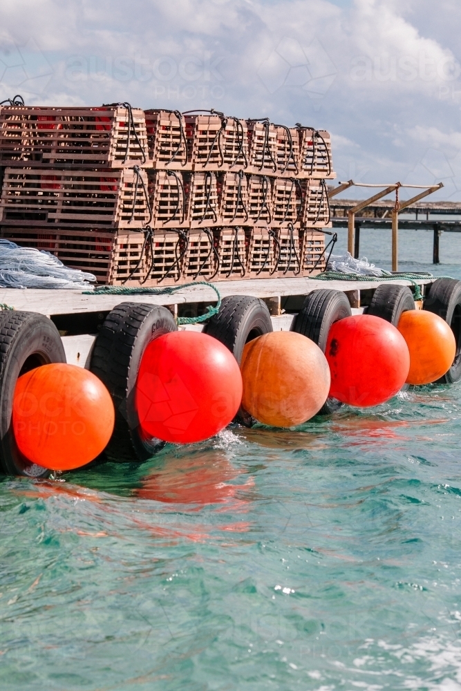 Commercial crayfishing with stacks of craypots and big orange buoys along the wooden jetty - Australian Stock Image