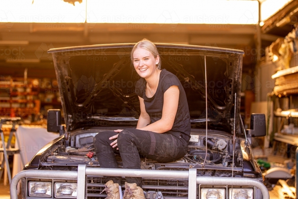 confident female mechanic sitting on a 4wd she has been working on in garage repair shop - Australian Stock Image