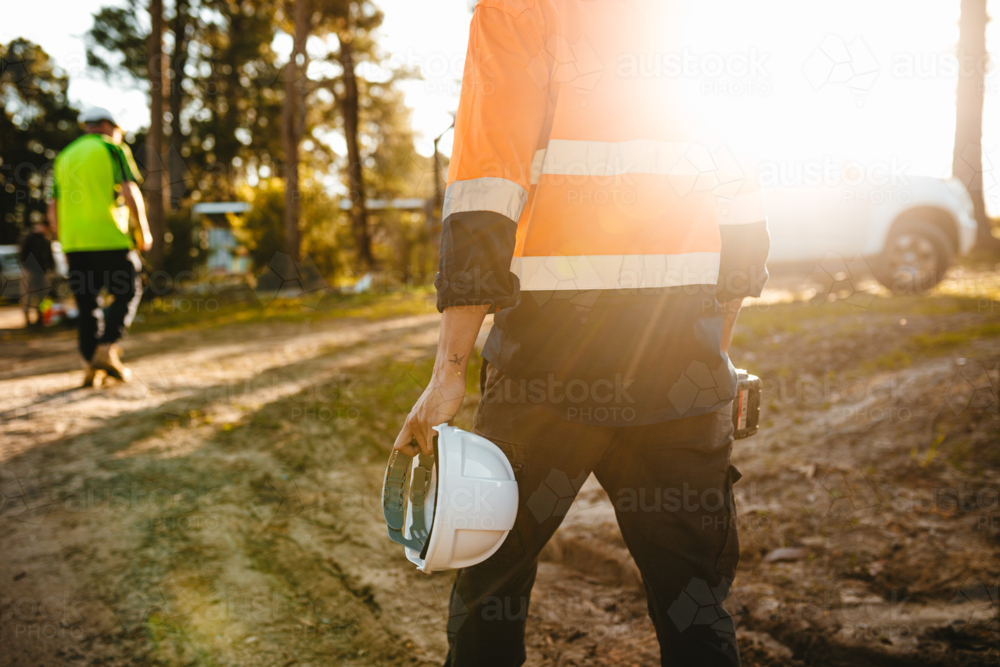 Construction worker holding a helmet and a drill while walking on the construction site. - Australian Stock Image