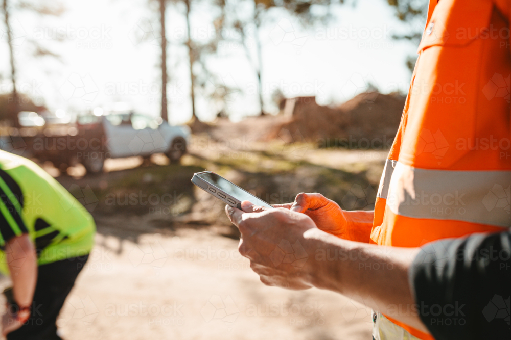 Construction worker holding a mobile device at the construction site. - Australian Stock Image