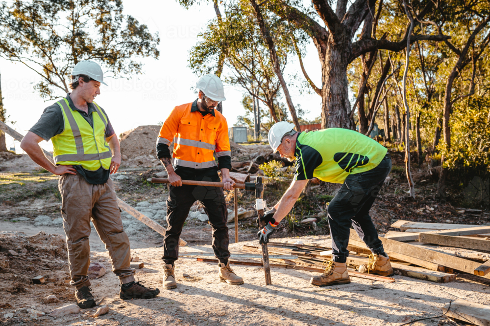 Construction workers driving a metal stake into the ground at construction site - Australian Stock Image