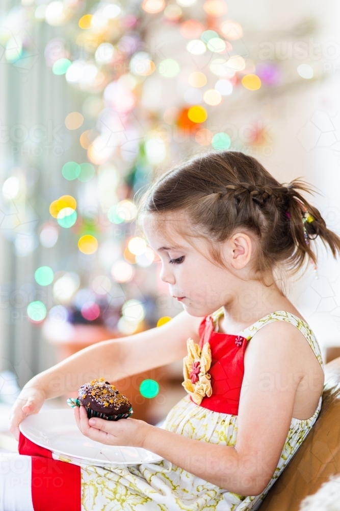 Content little girl eating a cupcake at Christmas time - Australian Stock Image