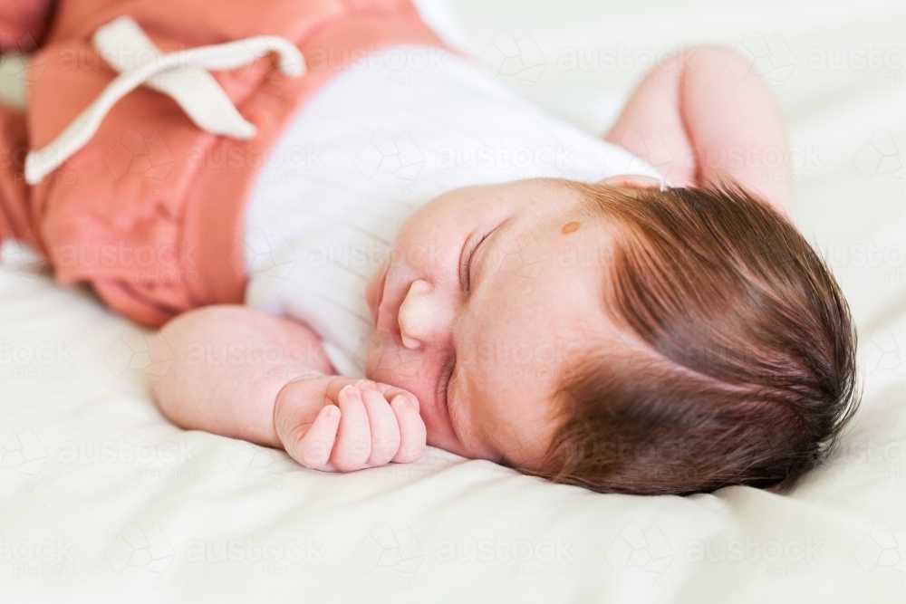 Content sleepy newborn baby with lots of hair lying on bed - Australian Stock Image