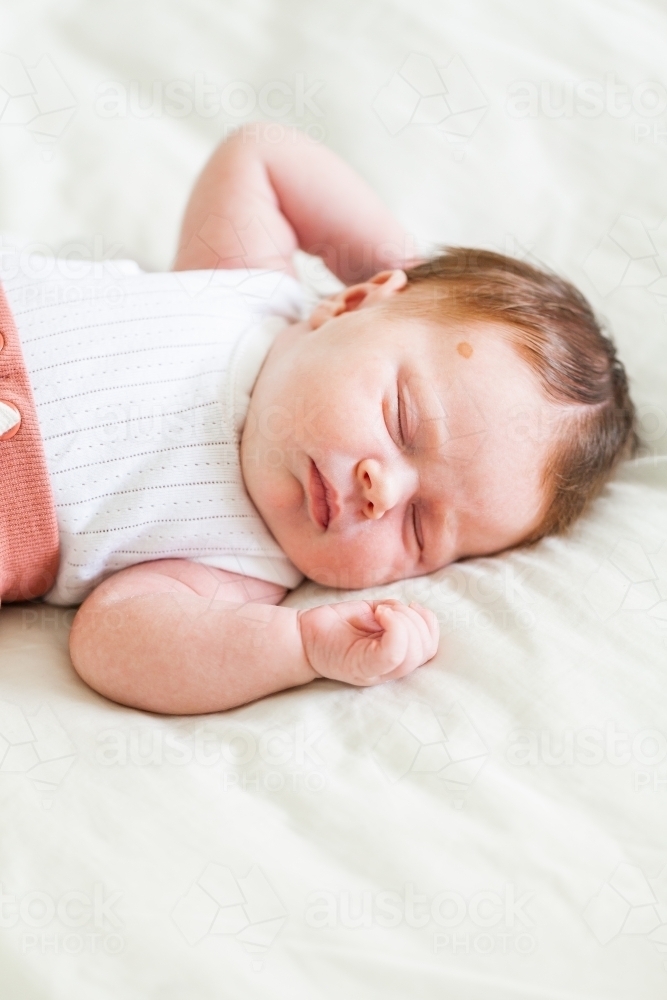 Content sleepy newborn baby with lots of hair lying on bed - Australian Stock Image