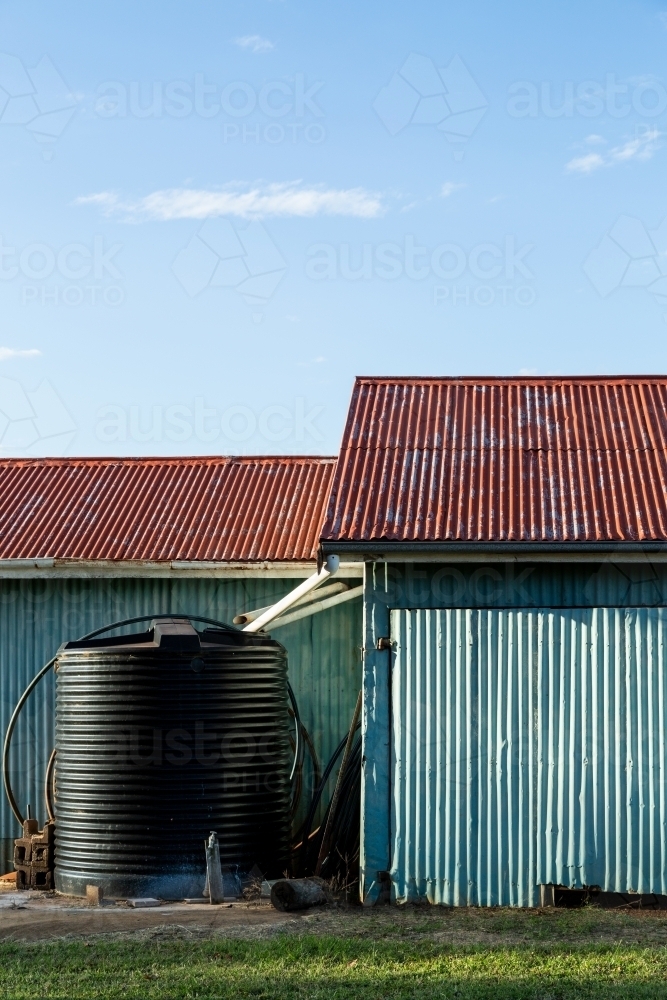 Corrugated iron farm shed painted blue, with red roof, and water tank. - Australian Stock Image