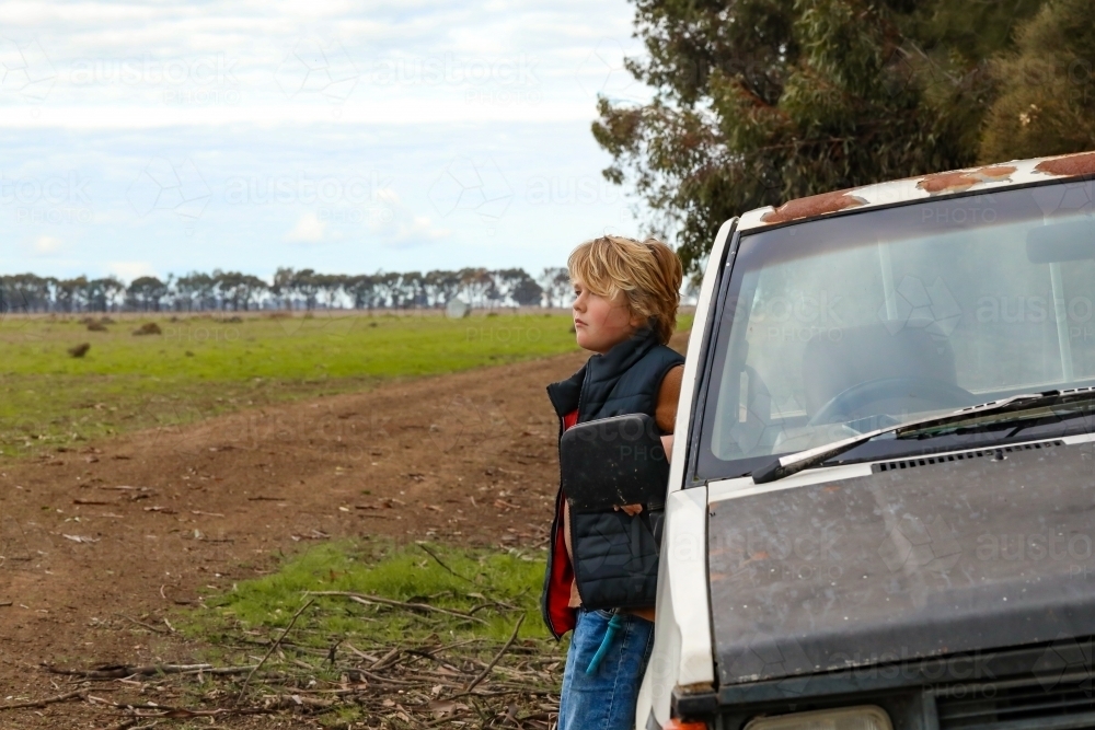 Country boy leaning against old farm ute in paddock - Australian Stock Image