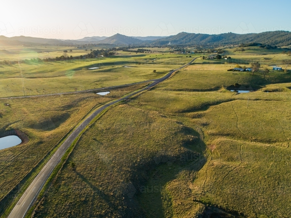 Country road dividing into two in green farmland at sunset - Australian Stock Image