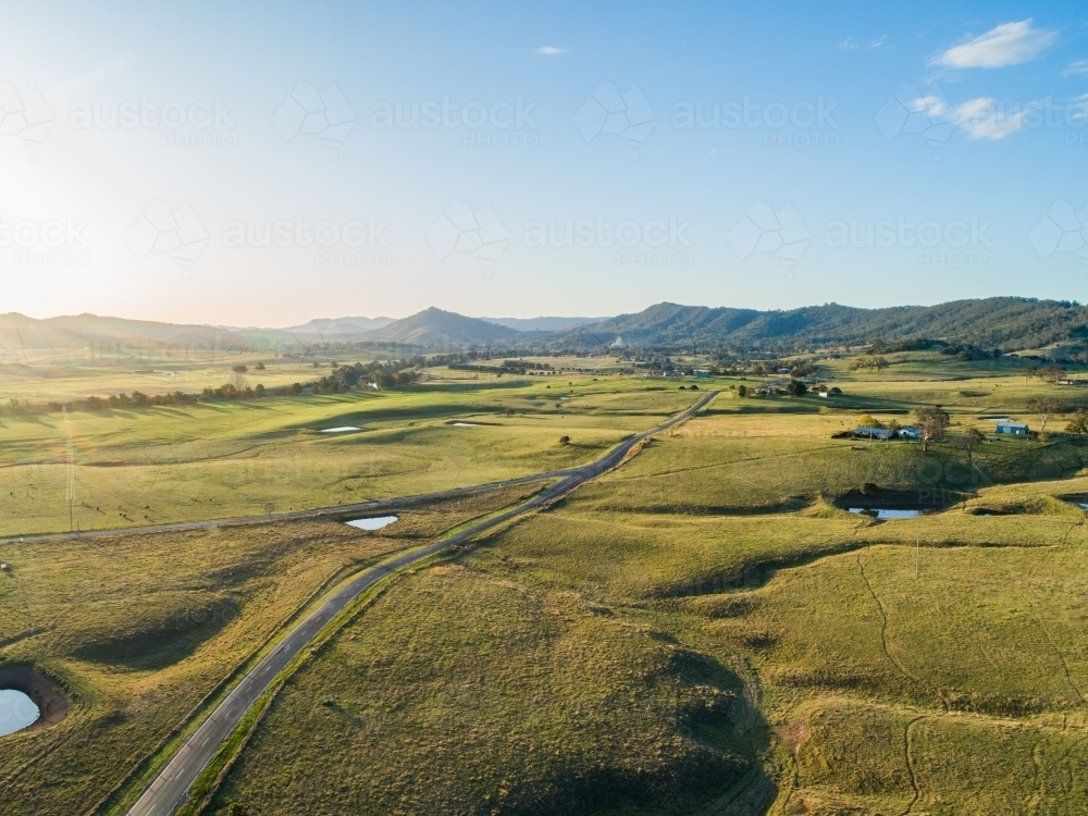 Country road dividing into two in green farmland at sunset - Australian Stock Image