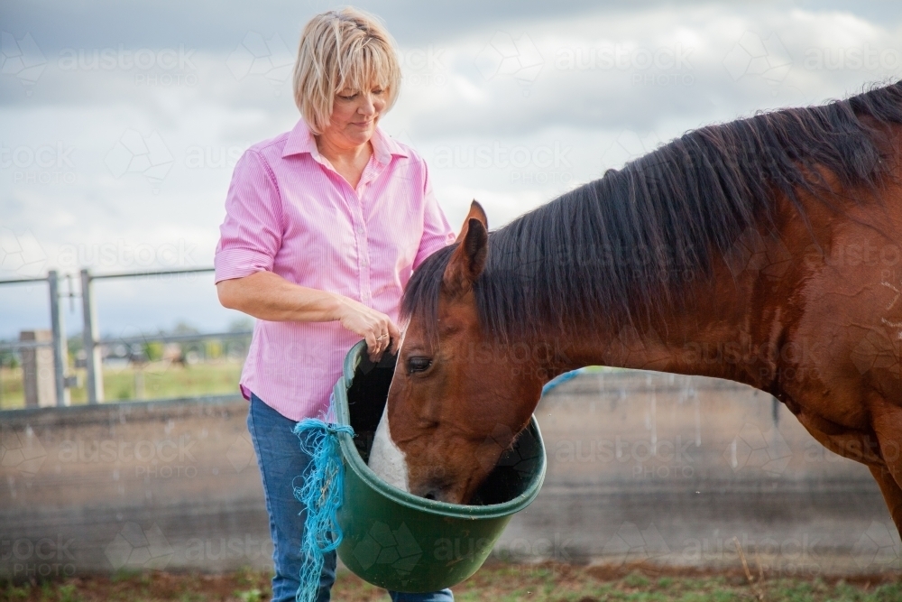 Country woman feeding her horse in round yard - Australian Stock Image