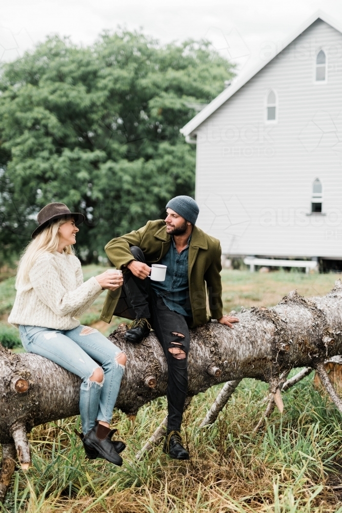 Couple sitting on fallen tree, talking and drinking coffee - Australian Stock Image