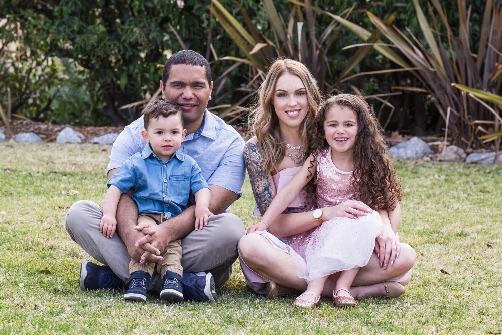 Couple sitting with son and daughter in lap smiling in garden - Australian Stock Image