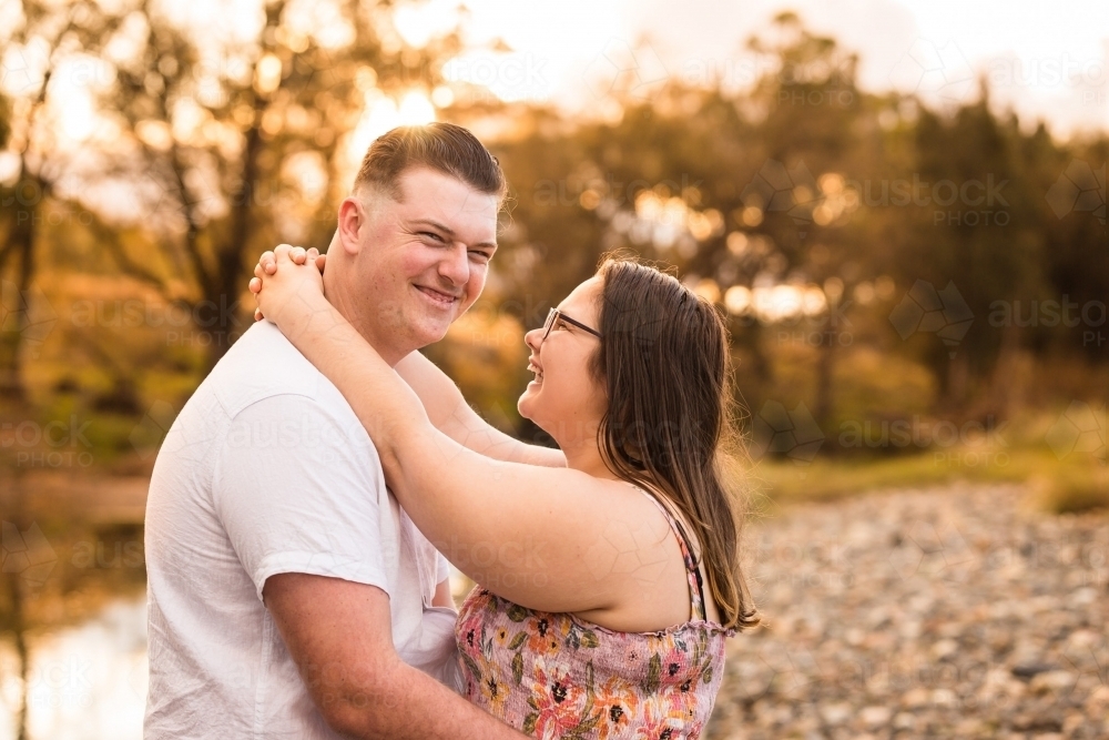 Couple standing with arms around each other woman laughing happy - Australian Stock Image