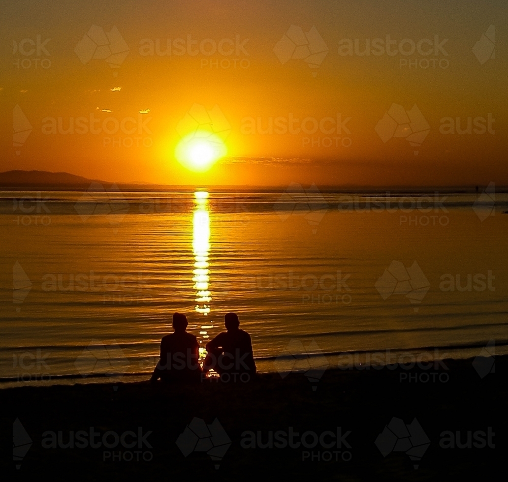 Couple watching the sunset over the water - Australian Stock Image