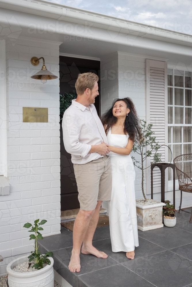 Couple wearing white standing together on front porch - Australian Stock Image