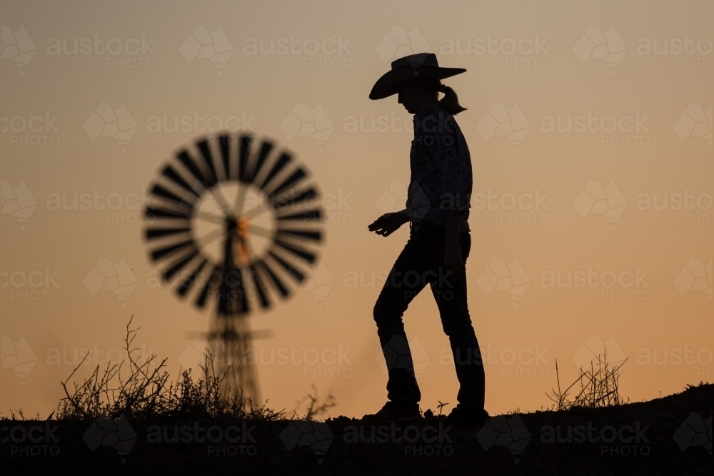 Cow girl and windmill at sunset - Australian Stock Image