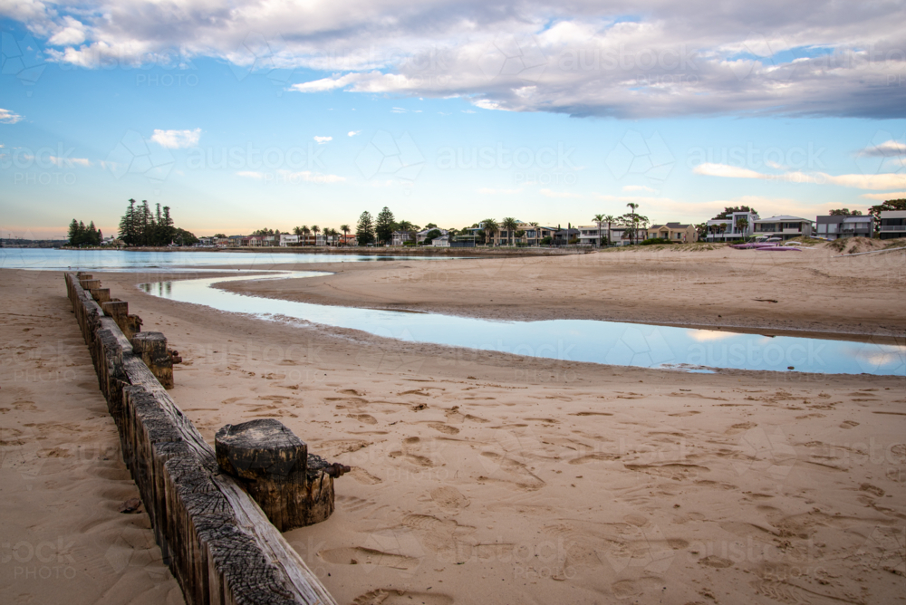 Creek flowing out to the bay past a wooden fence - Australian Stock Image