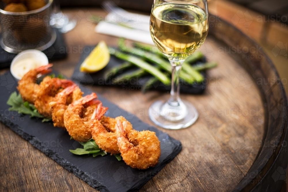 crispy fried shrimp tempura served on a black slate plate with a glass of white wine - Australian Stock Image