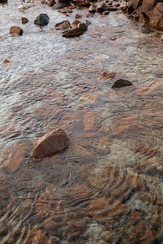 Crystal clear water flowing over a bed of reddish-brown rocks - Australian Stock Image