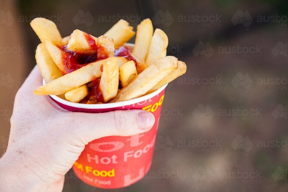 Cup of hot chips and tomato sauce held in hand at sports event - Australian Stock Image