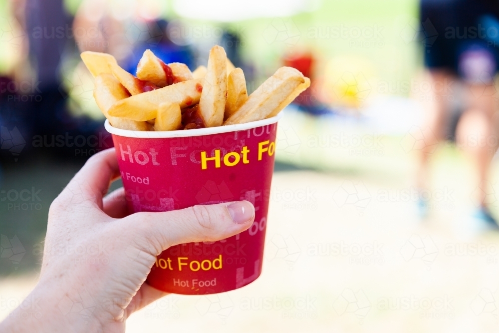 Cup of hot chips and tomato sauce held in hand at sports event - Australian Stock Image