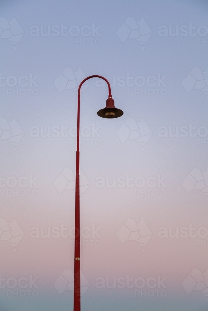 Curved red lamp post against pastel gradient of dusk sky - Australian Stock Image