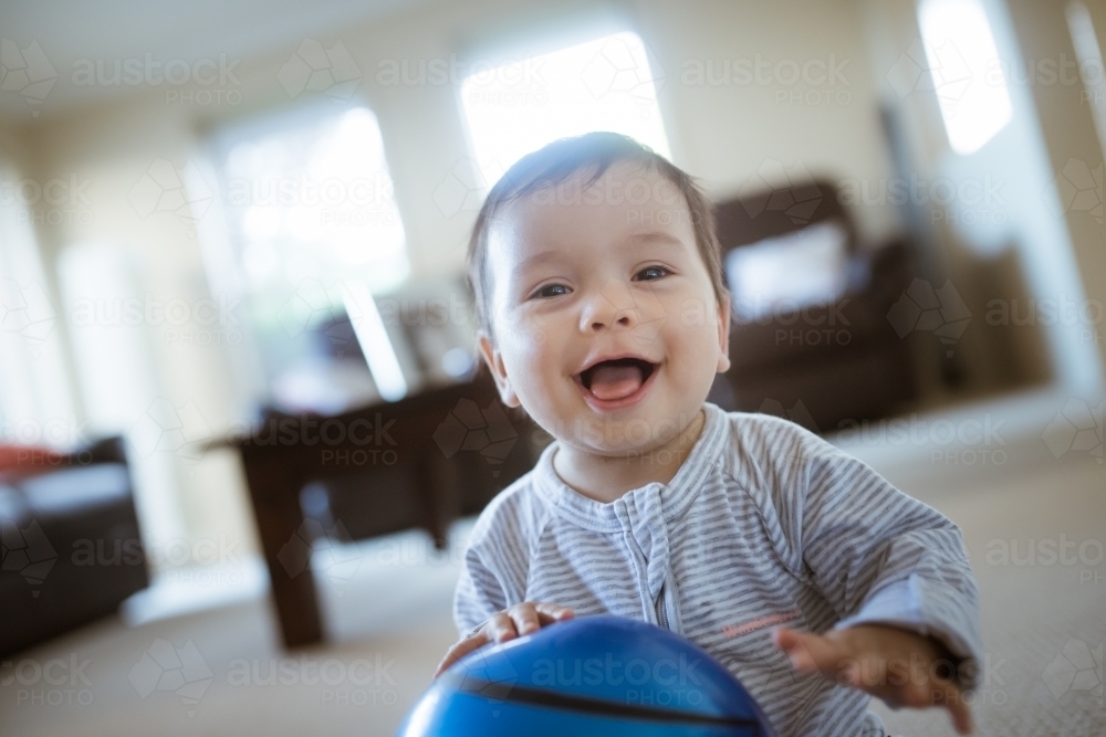 Cute 1 year old mixed race boy plays at home with a smiley face ball - Australian Stock Image