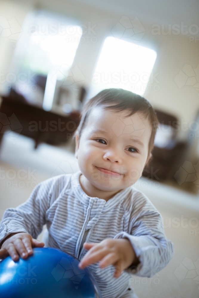 Cute 1 year old mixed race boy plays at home with a smiley face ball - Australian Stock Image