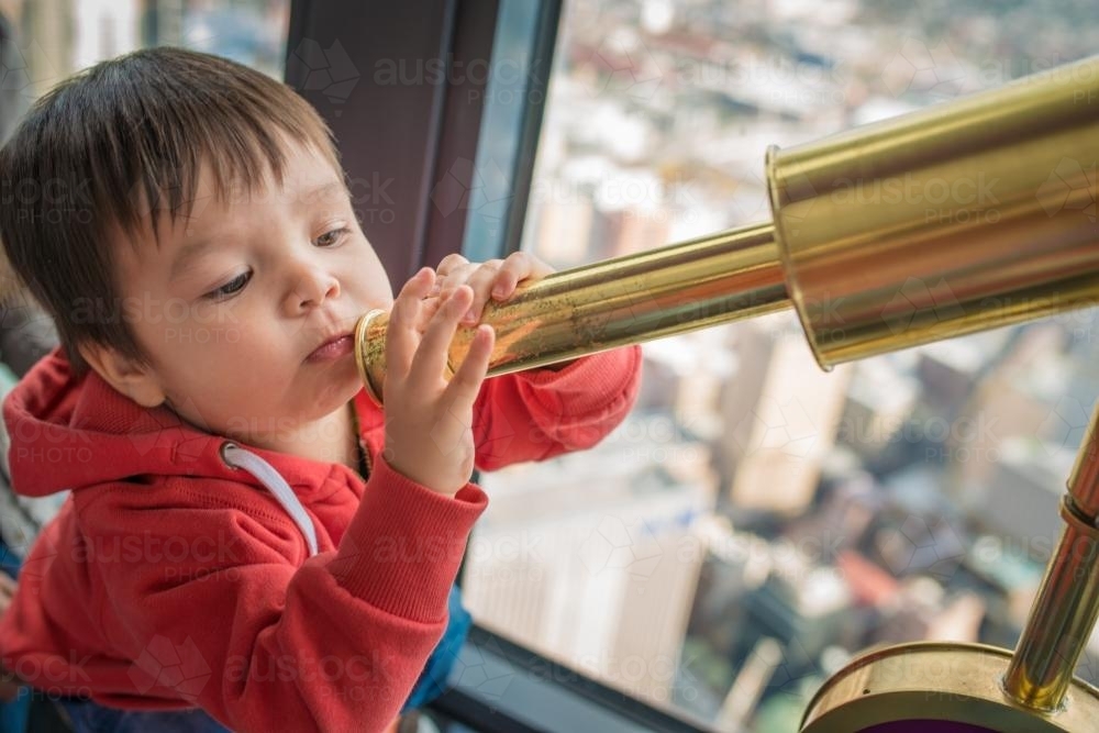 Cute 2 year old mixed race boy plays with a telescope in Sydney Centrepoint Tower - Australian Stock Image